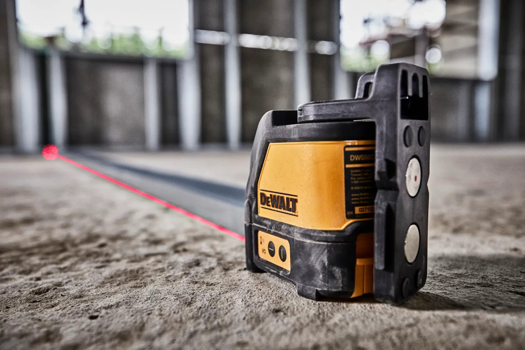 DEWALT DW088K laser level projects a red line across a construction floor for precise alignment.