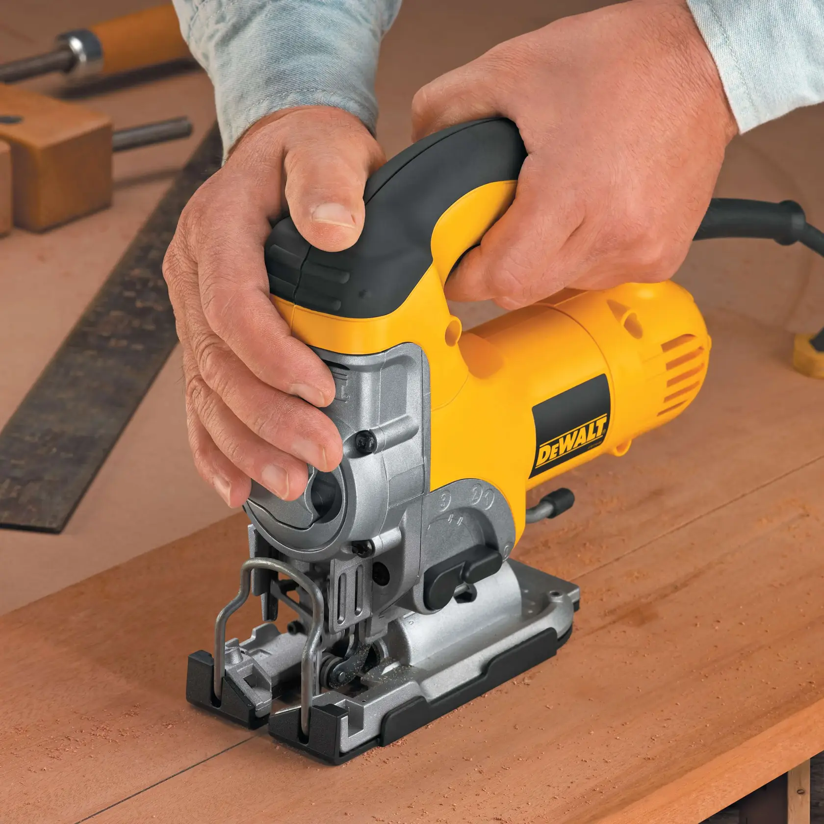 Close-up view of hands using a yellow and black DEWALT electric jigsaw to cut through a dark sheet of material.