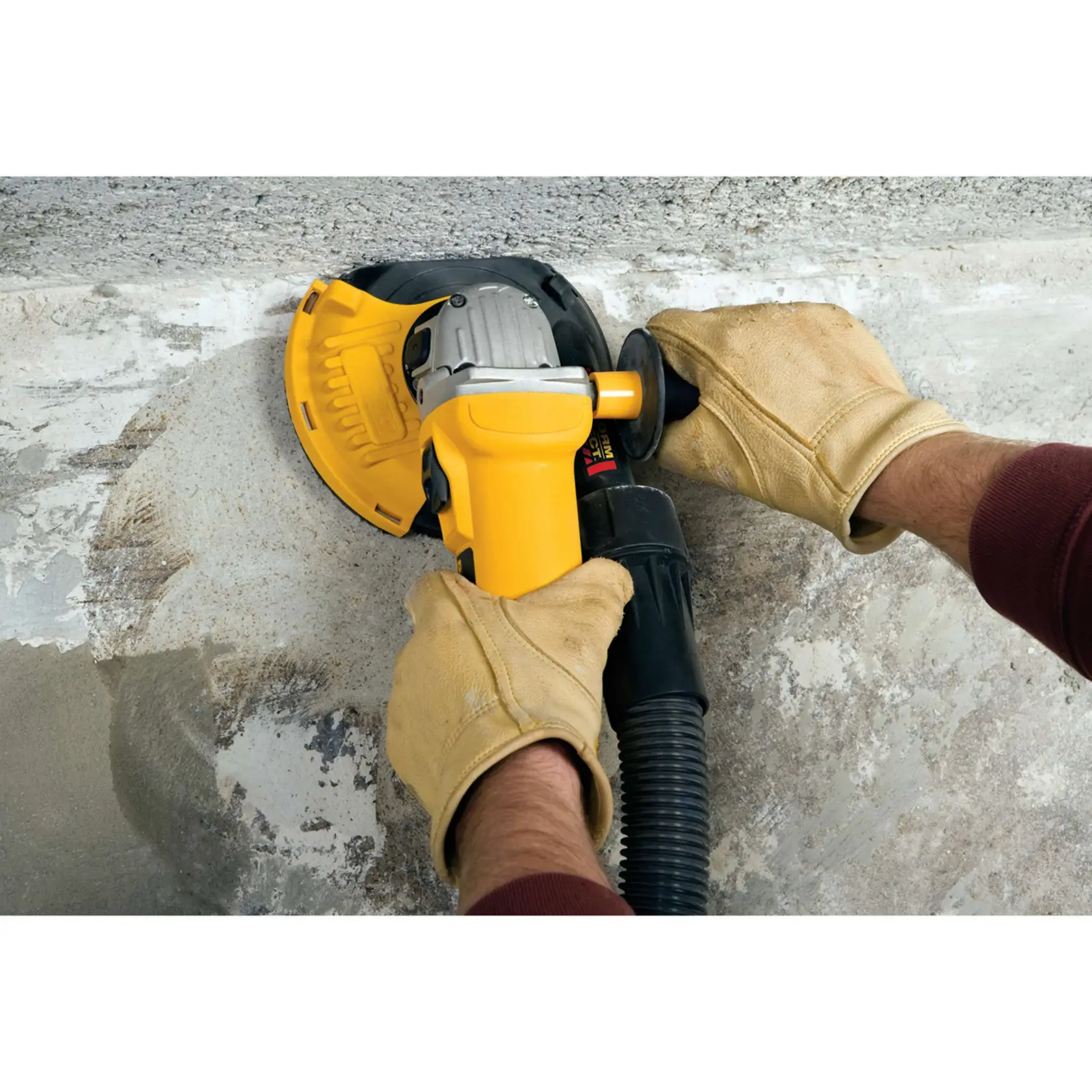 Primer plano de manos con guantes utilizando una herramienta eléctrica amarilla DEWALT para pulir y alisar una superficie de concreto.