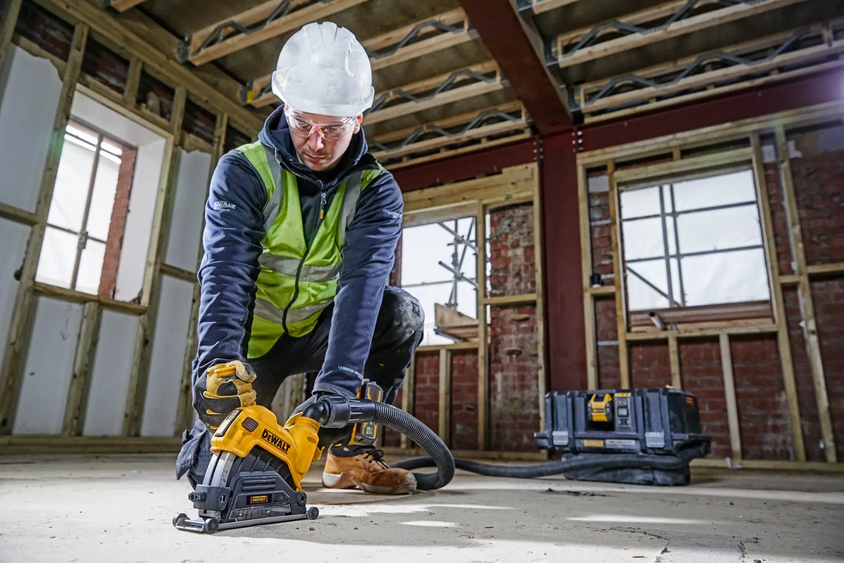 Trabajador usa DEWALT DWE46225 en obra, con equipo de seguridad, cortando el suelo de concreto.