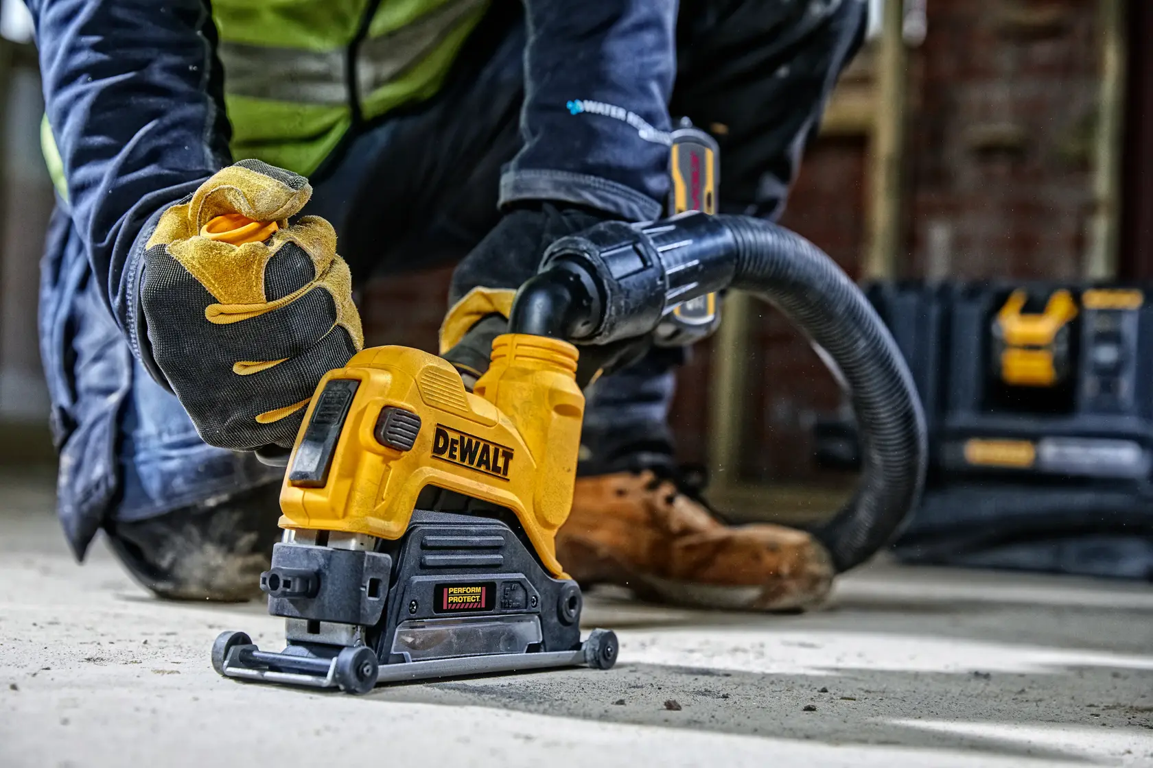Trabajador usa herramienta DEWALT DWE46225 con extractor de polvo en piso de concreto en obra.