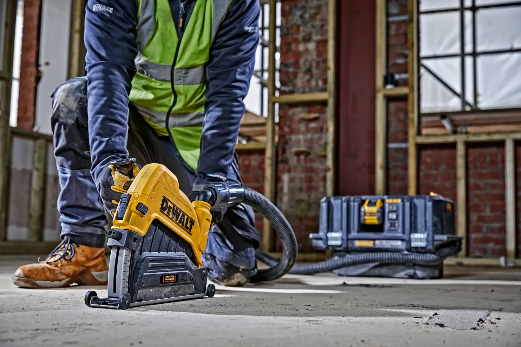 Persona usando ranuradora DEWALT en suelo de concreto en obra. Caja de herramienta visible atrás.