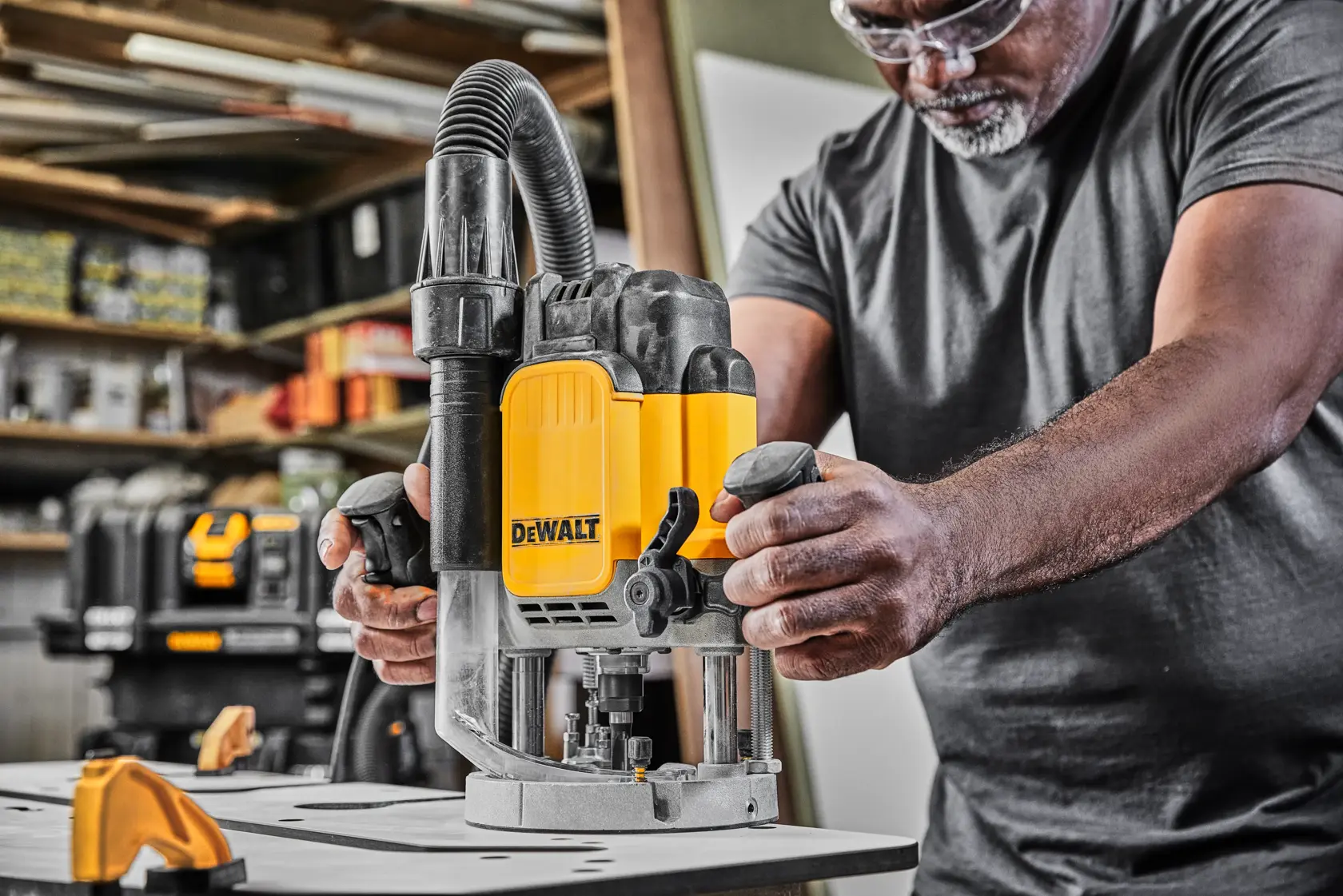 Person using a DEWALT router tool on a workbench in a workshop setting.
