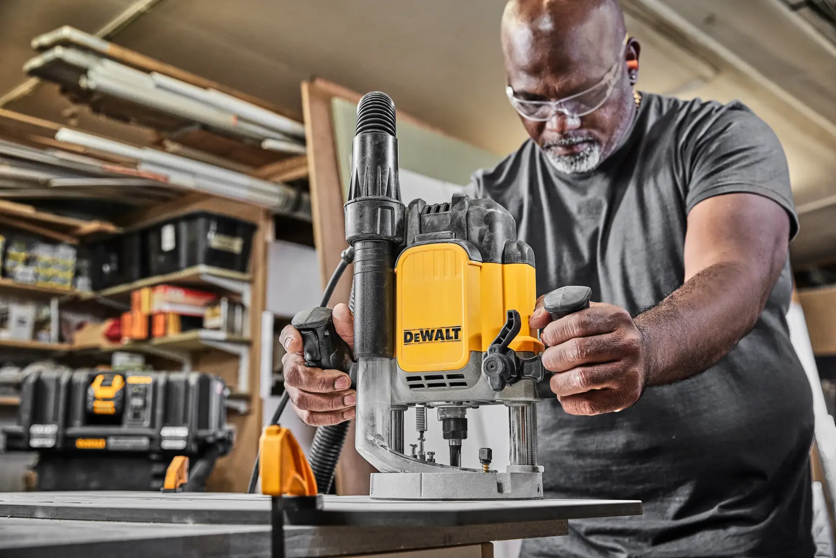 Person using DEWALT DWE625KT plunge router tool on a workbench in a workshop setting.