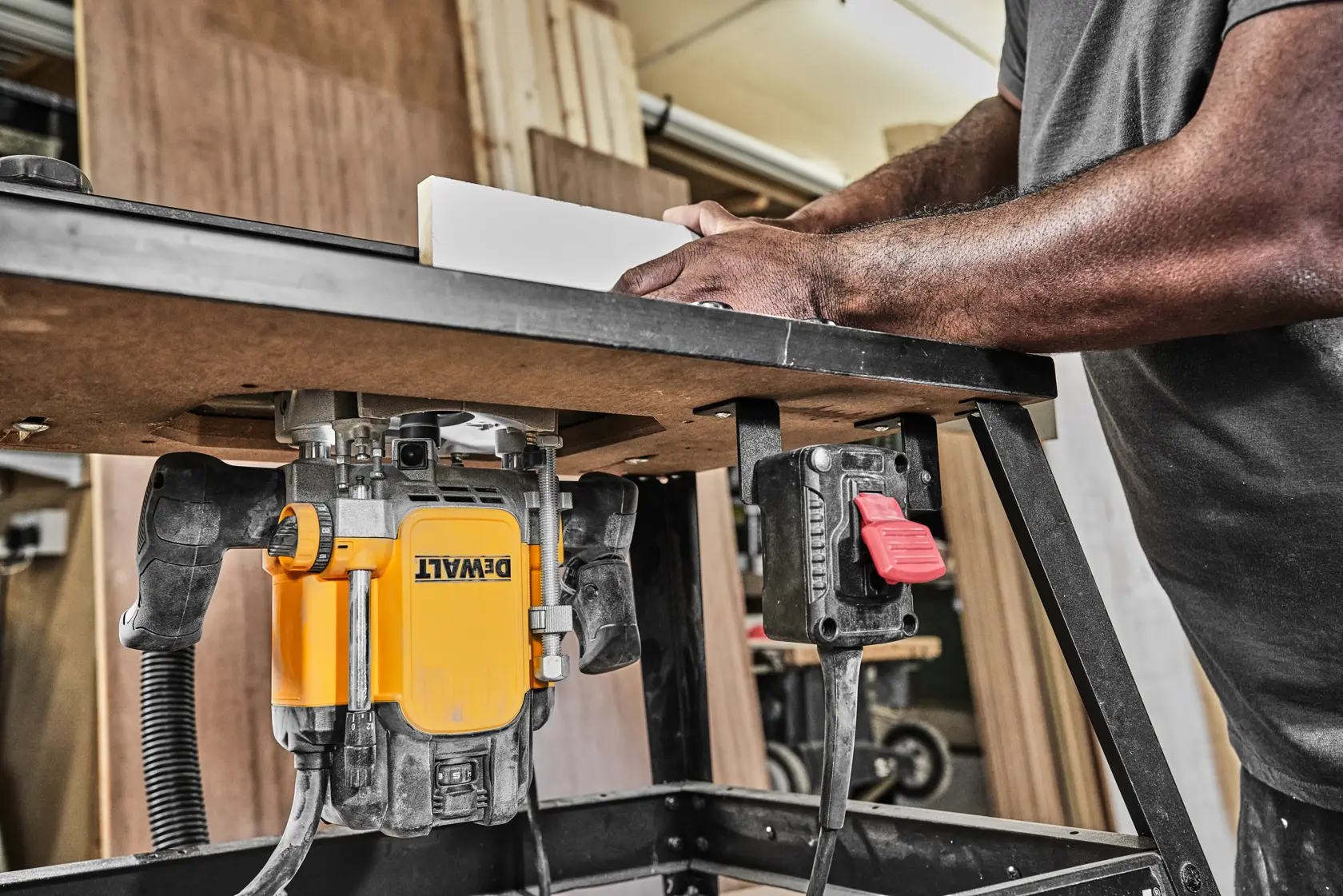 Fresadora DEWALT montada en mesa, manos guiando madera en taller.