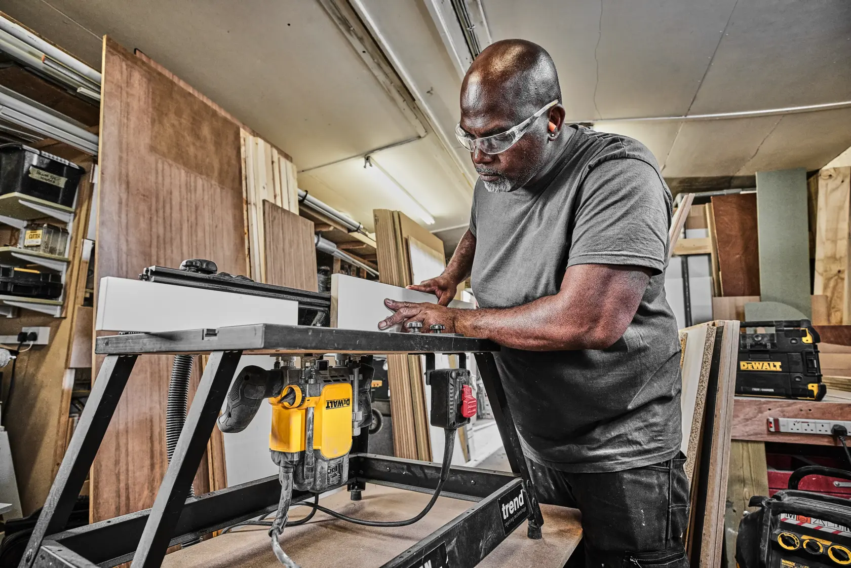 Persona usa una fresadora DEWALT en un taller, trabajando madera sobre una mesa resistente.