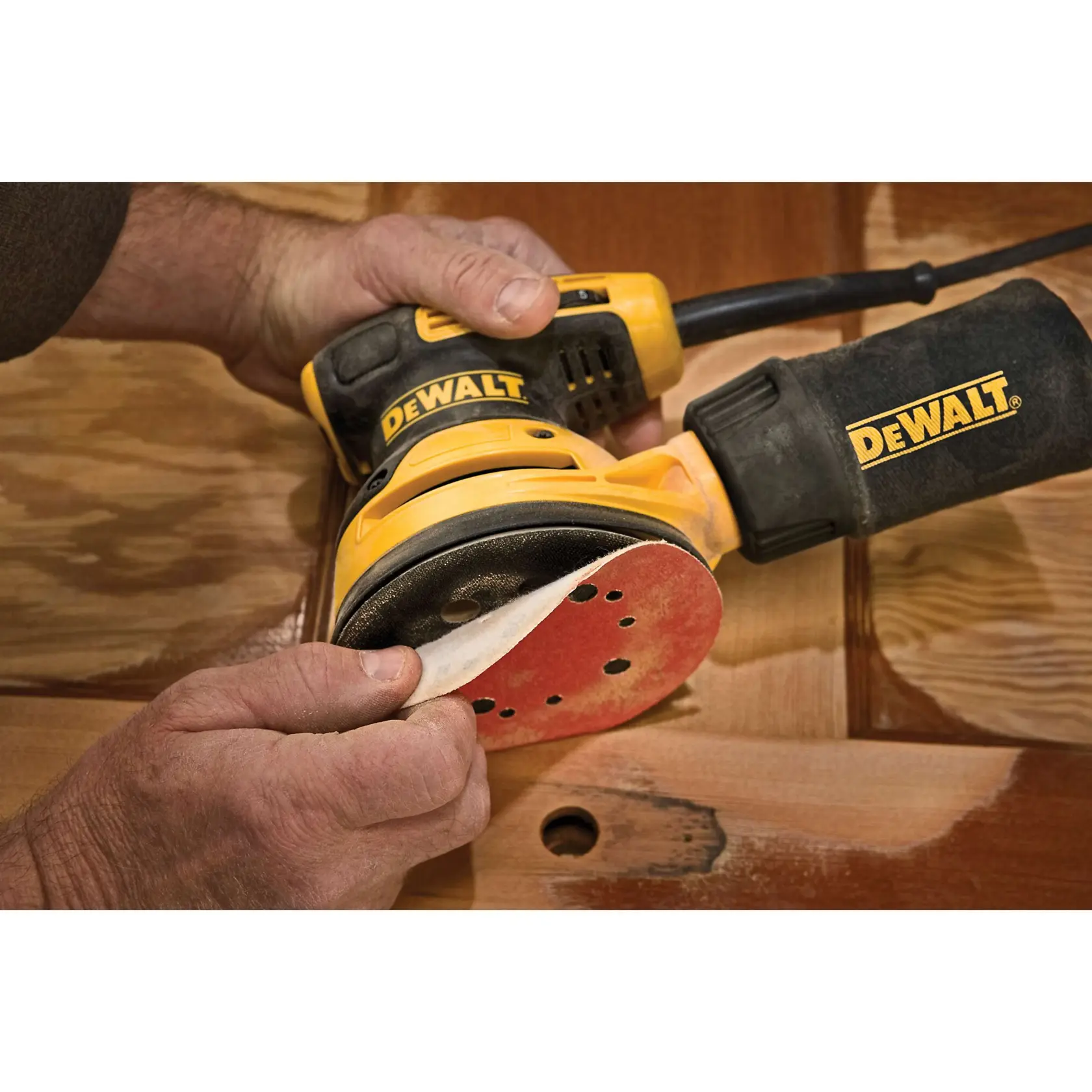 DEWALT electric orbital sander with a dust bag, featuring a yellow and black design. Text below reads: 'Steady control with rubber overmold grip.'