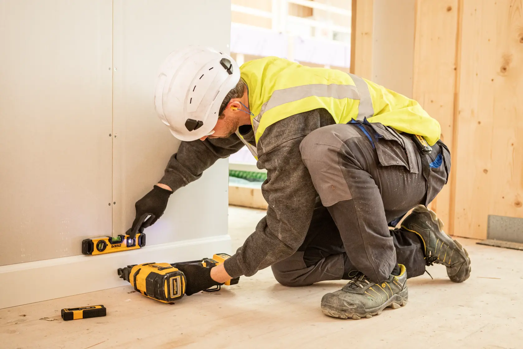 Trabajador usa herramientas DEWALT y nivel para instalar una pared en obra.