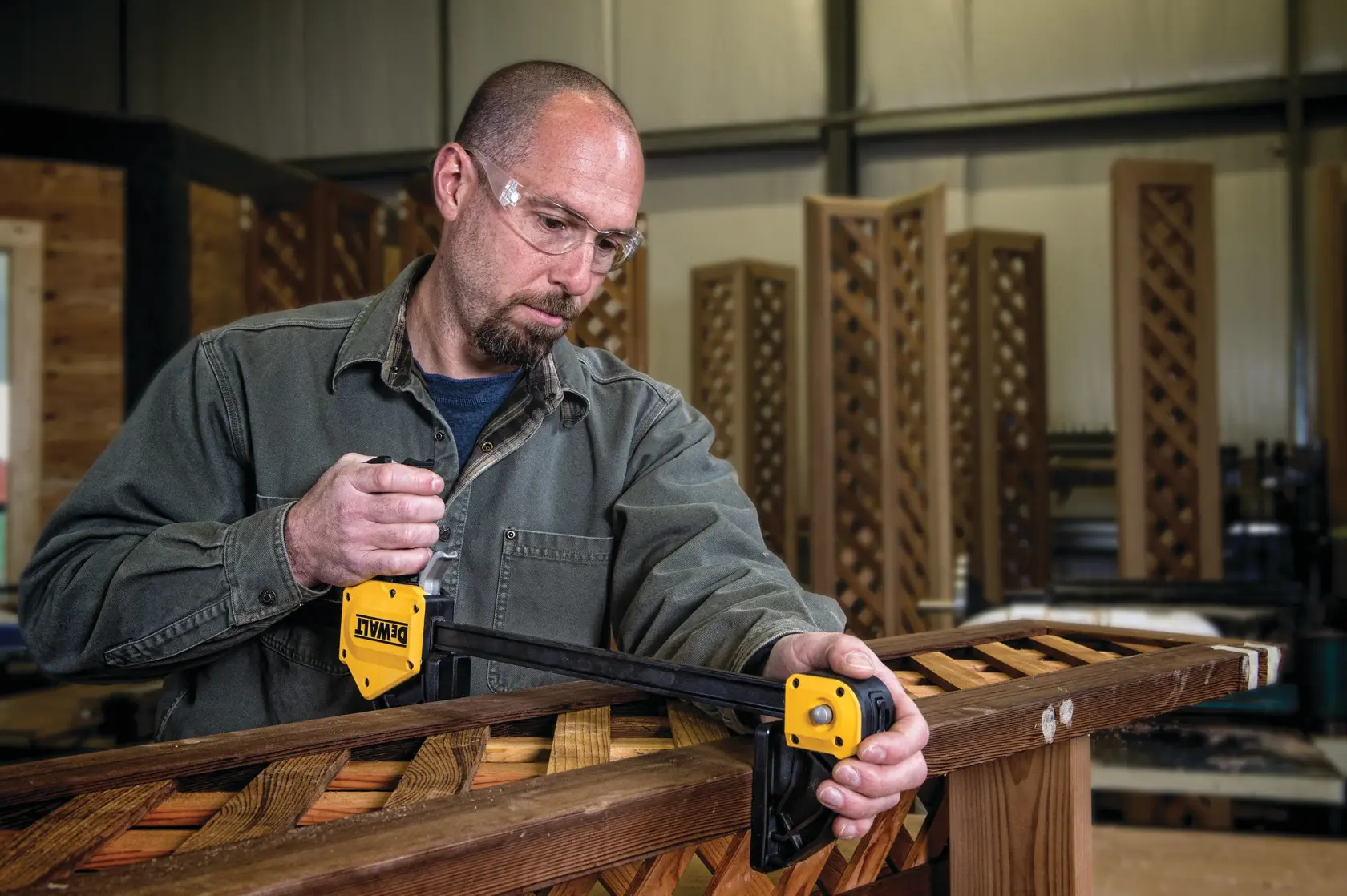 Persona usando una prensa DEWALT para sujetar tablas de madera en un taller.