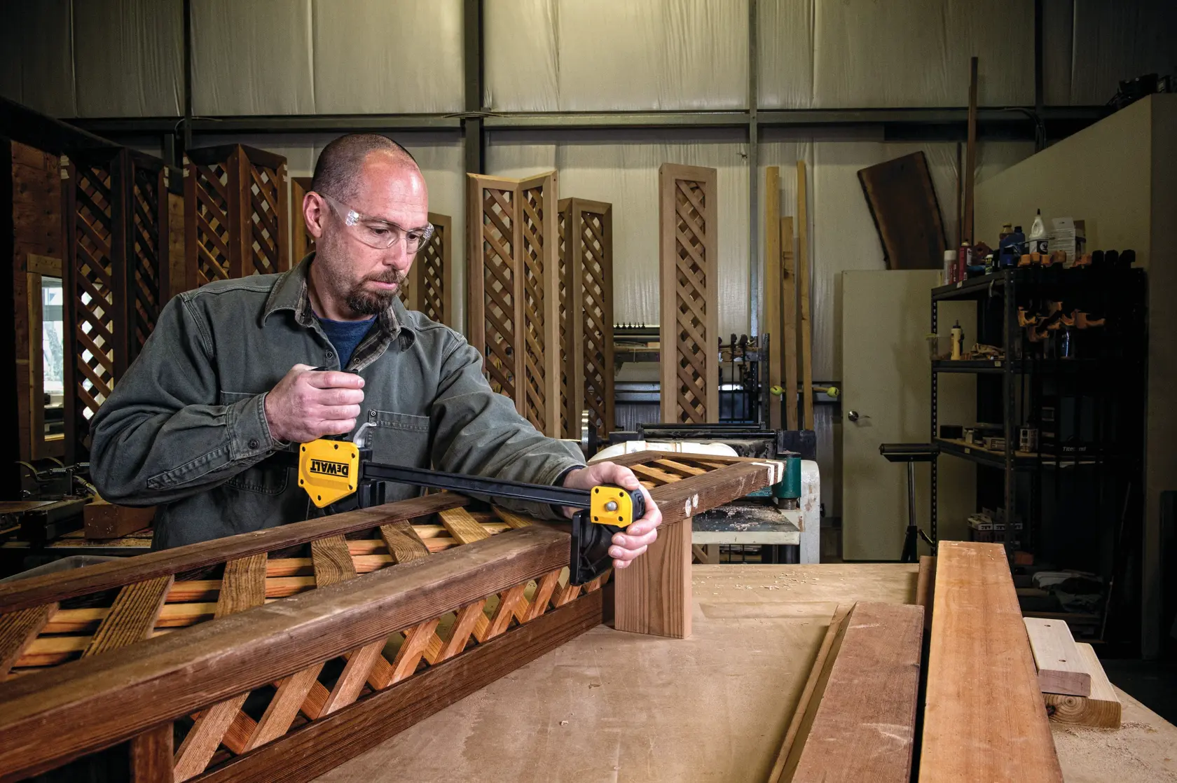 Persona usando una pinza DEWALT para sujetar piezas de madera en un taller con celosías visibles.