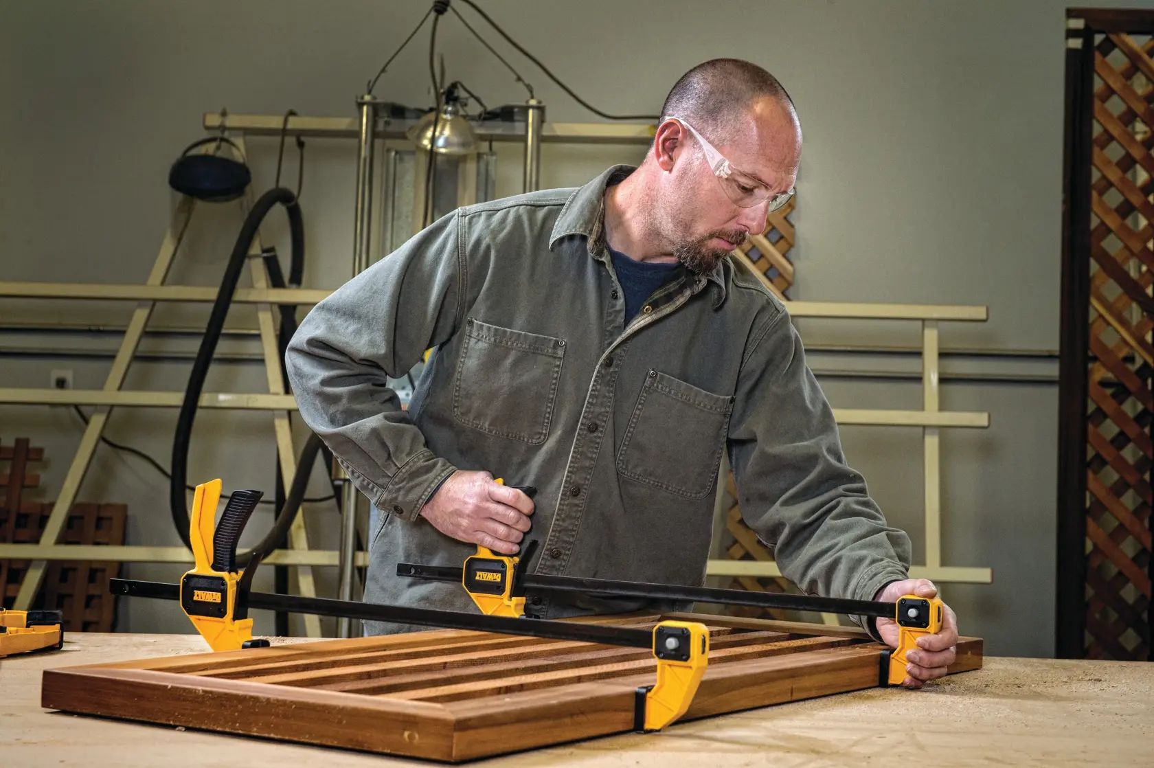 Persona usa sargentos DEWALT para fijar un panel de madera en una mesa de trabajo en taller.