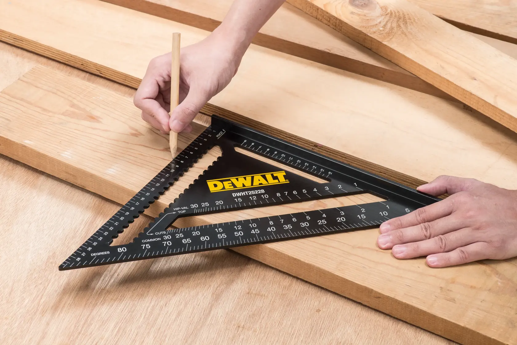 Una herramienta de escuadra de fotografía DEWALT DWHT25228-0 está colocada sobre tablas de madera. Una mano sostiene la herramienta y la otra usa un lápiz para marcar las medidas en la madera.