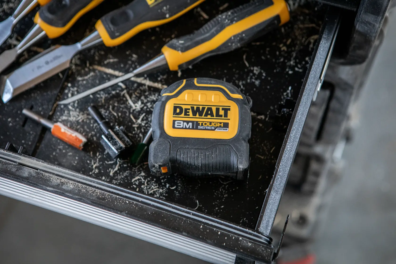 DEWALT 8m Maßband auf Werkbank mit Schraubendrehern und Werkzeug, umgeben von Holzspänen.