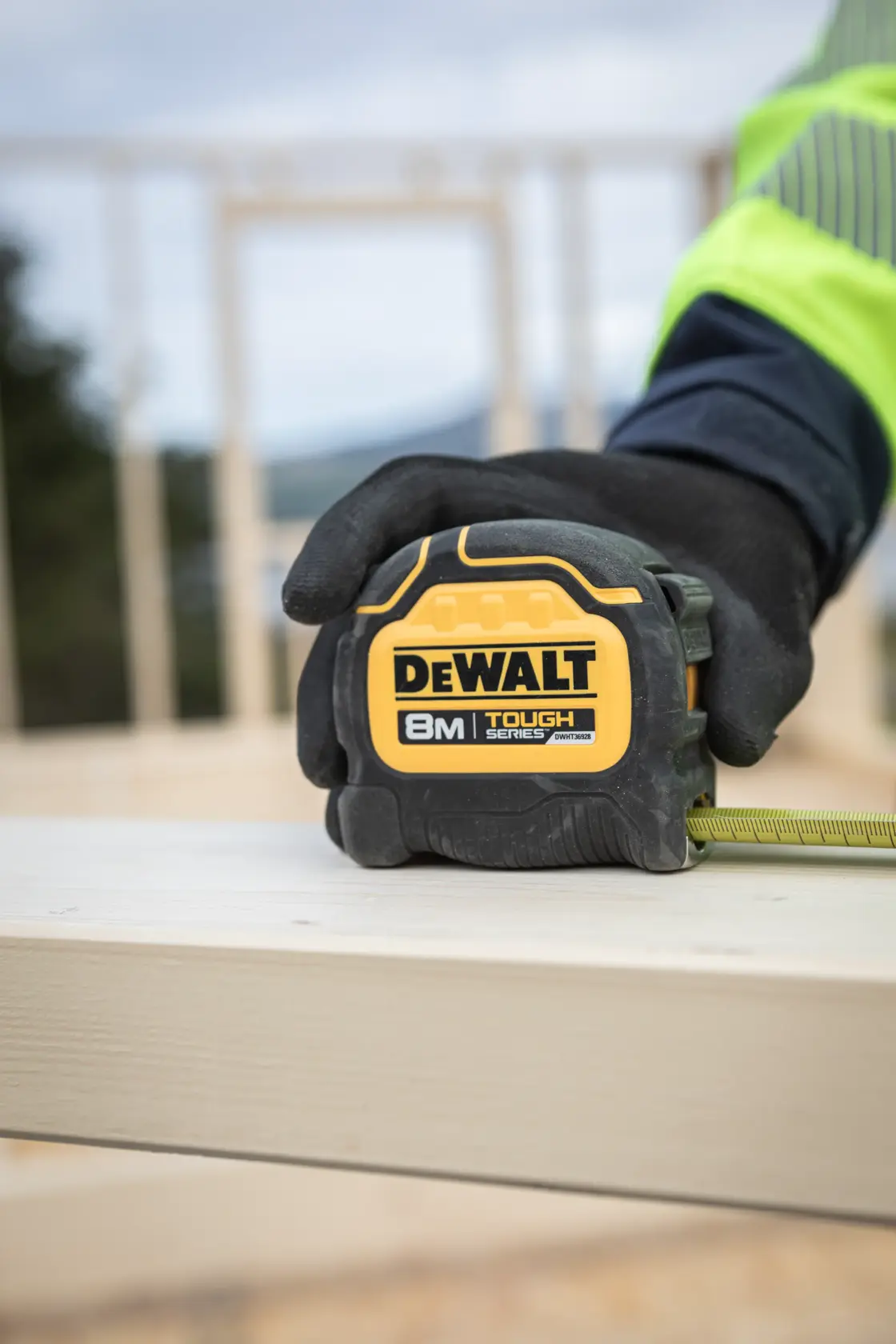 DEWALT 8M Tough Series Maßband wird von einer behandschuhten Hand auf einer Holzplanke gehalten.