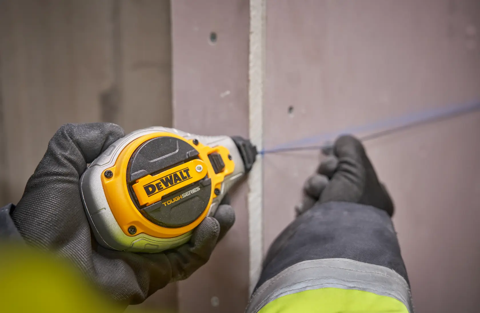 Gloved hand using a DEWALT ToughSeries chalk line tool on a drywall surface.