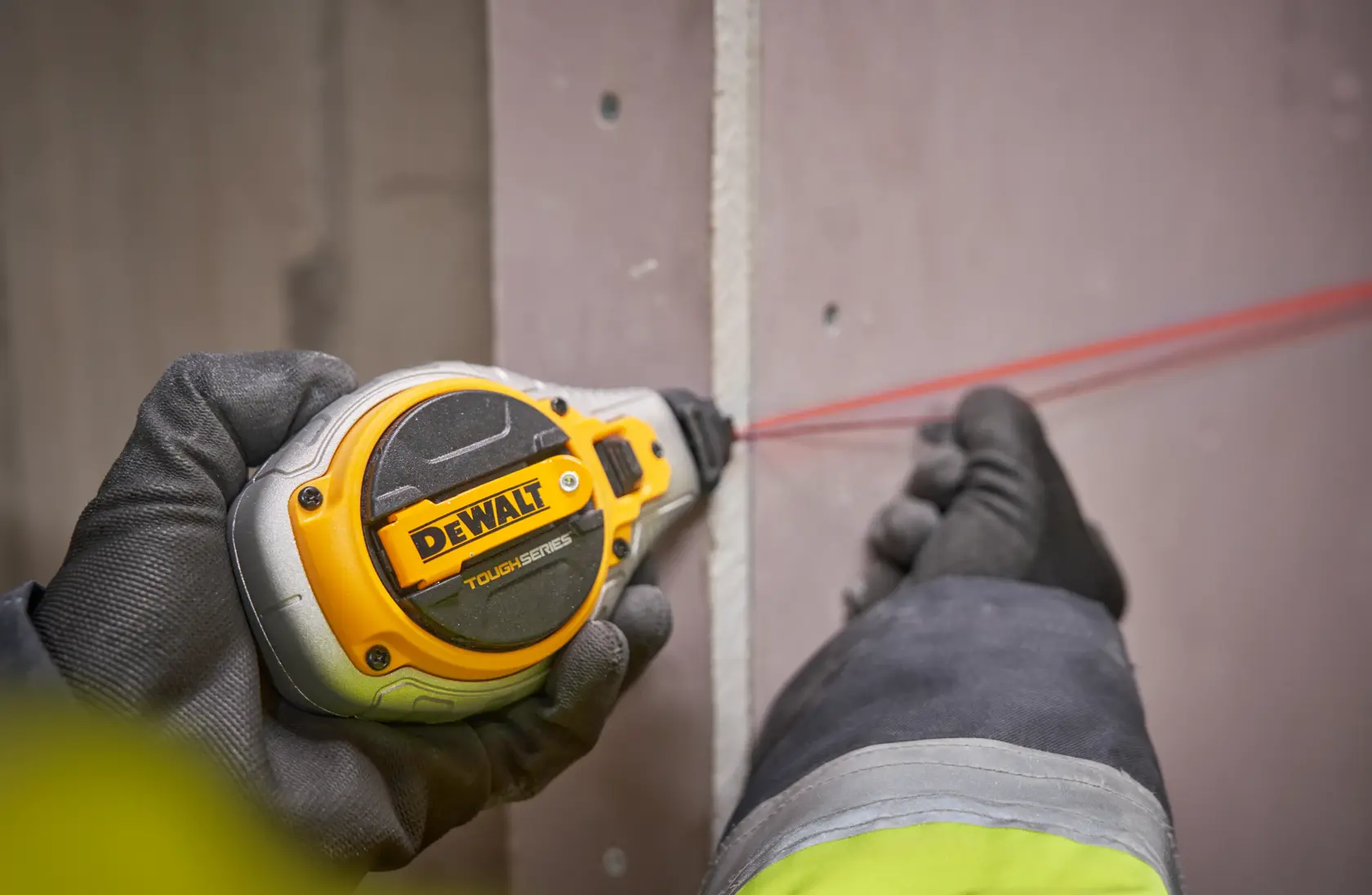 Manos con guantes usan una herramienta DEWALT ToughSeries para marcar una línea en una pared de yeso.