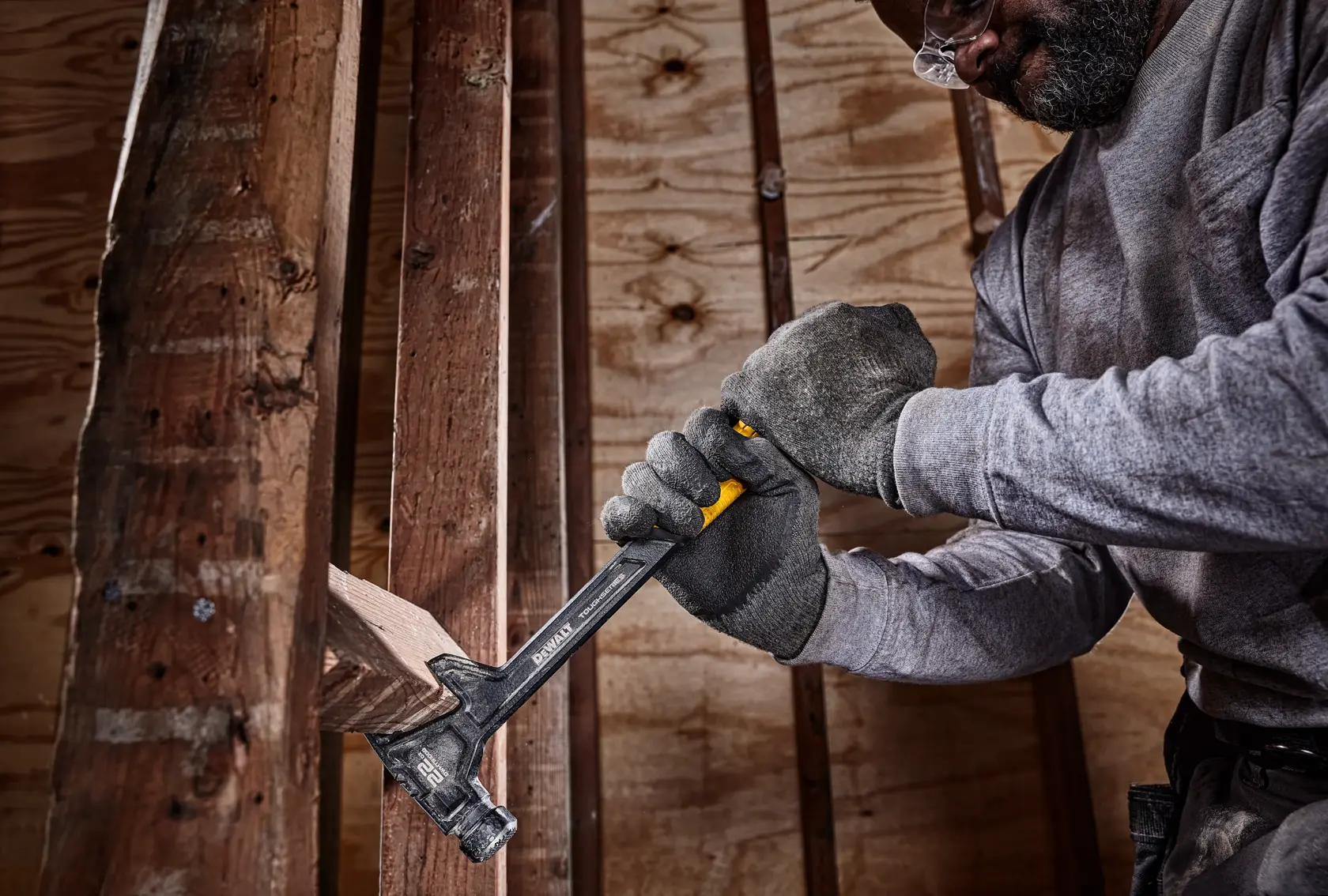 Eine Person mit Arbeitshandschuhen verwendet einen DEWALT Hammer, um ein Holzbrett auf einer Baustelle zu entfernen.