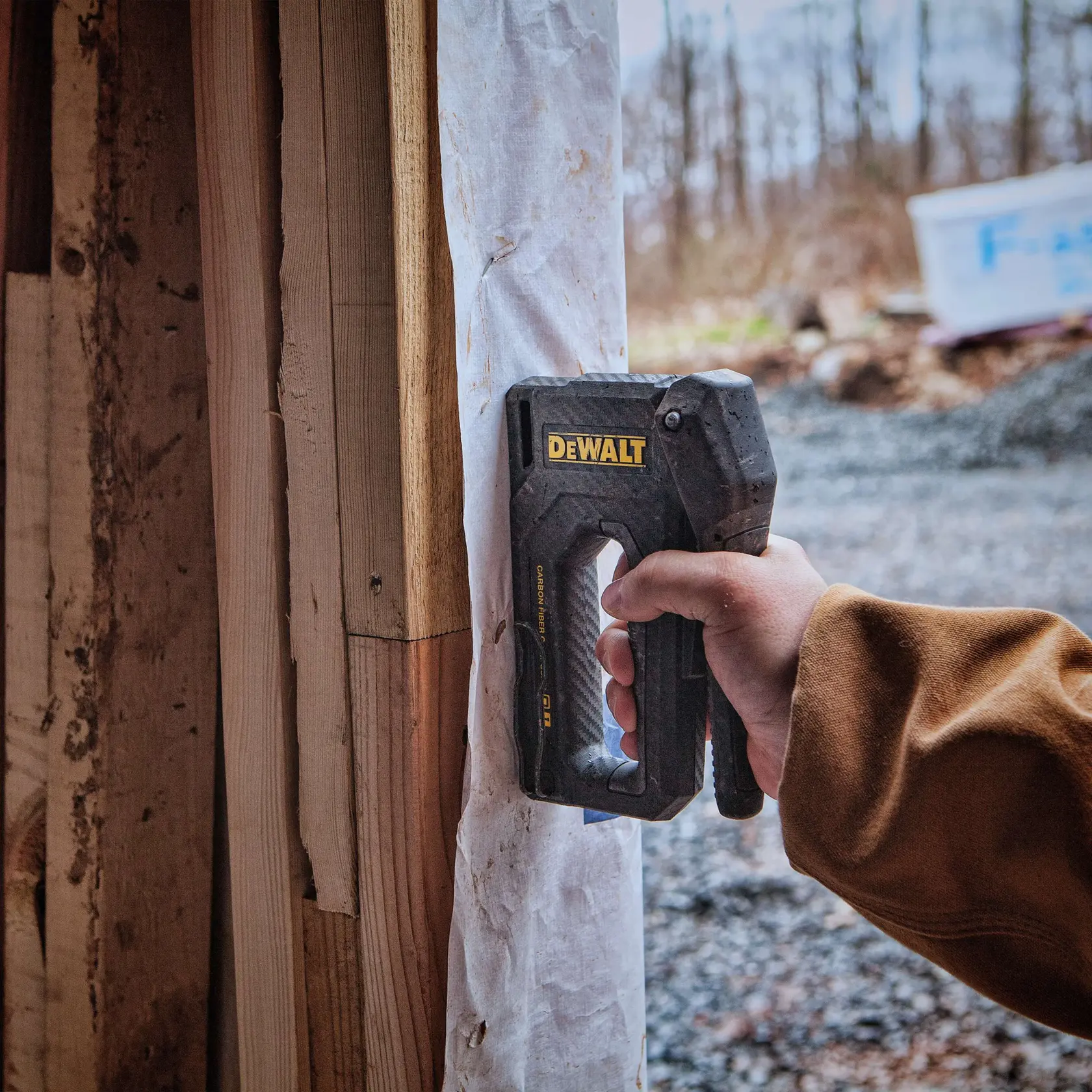 Eine Person benutzt einen DEWALT-Tacker, Modell DWHT80276, um ein Materialblatt an einem Holzrahmen auf einer Baustelle zu befestigen.
