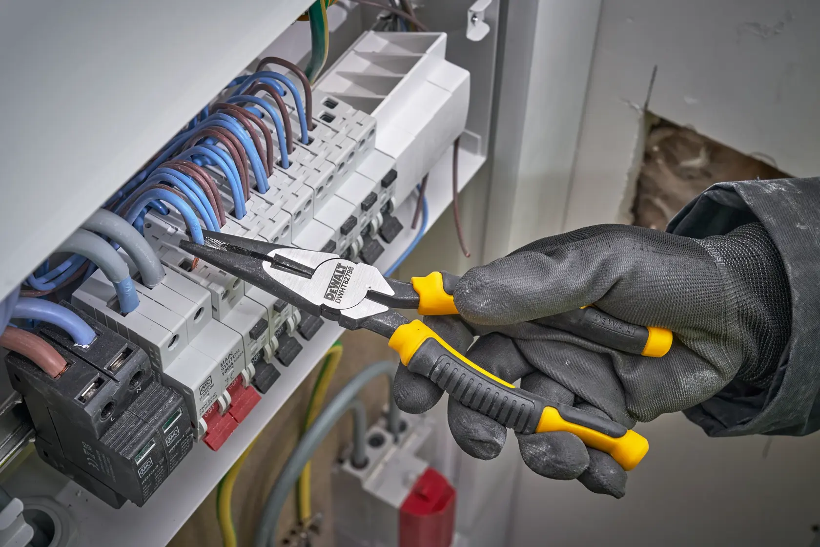 Gloved hand uses DEWALT pliers to grip electrical wires inside a circuit breaker panel.