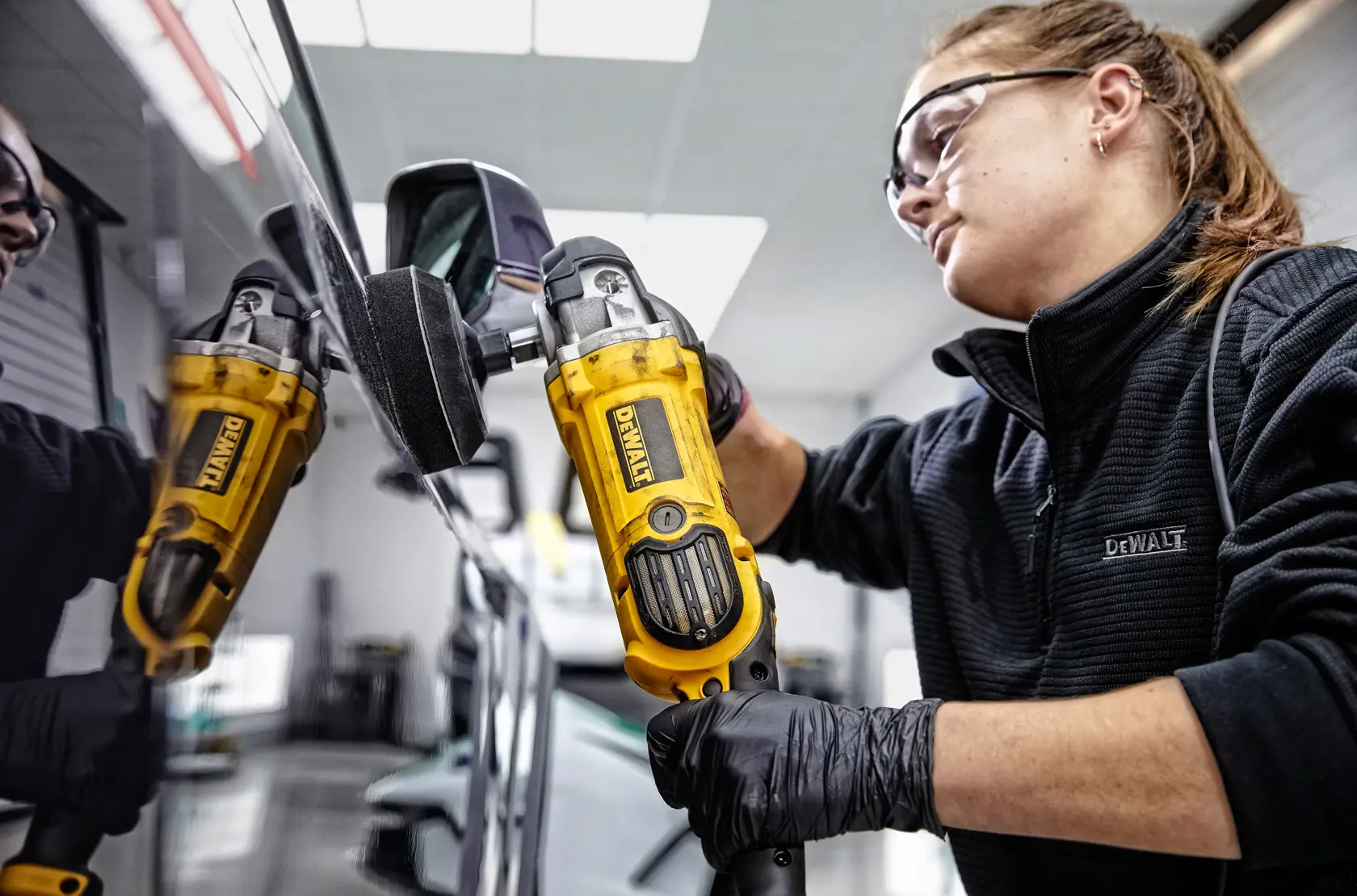 A person is polishing the hood of a red sports car with a DEWALT DWP849X polisher in a garage.