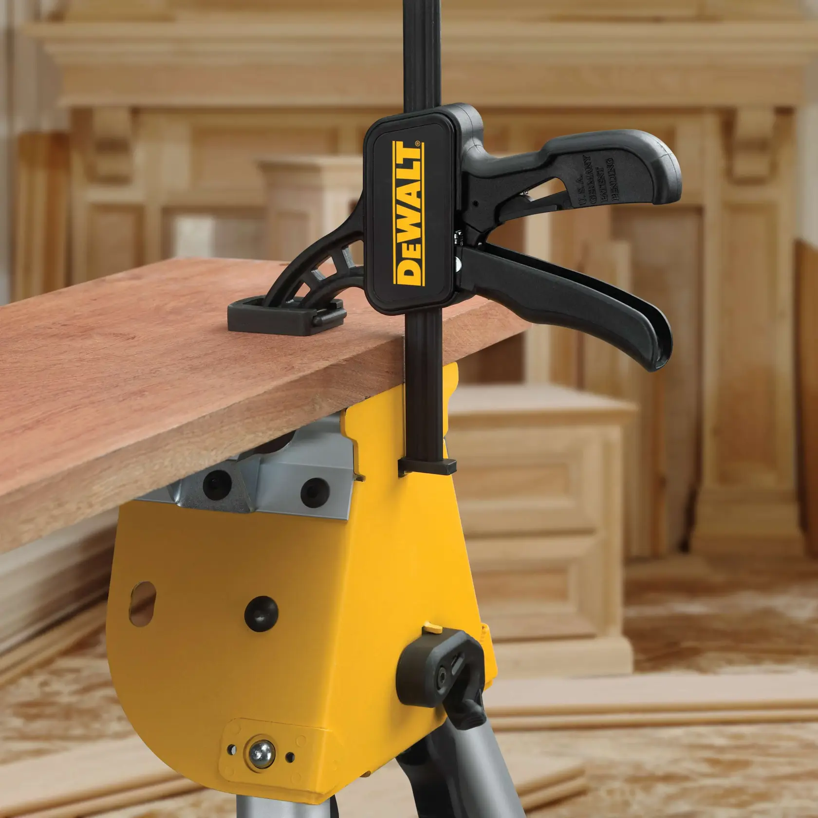 Pinza DEWALT sujeta una tabla de madera sobre banco amarillo en un taller.