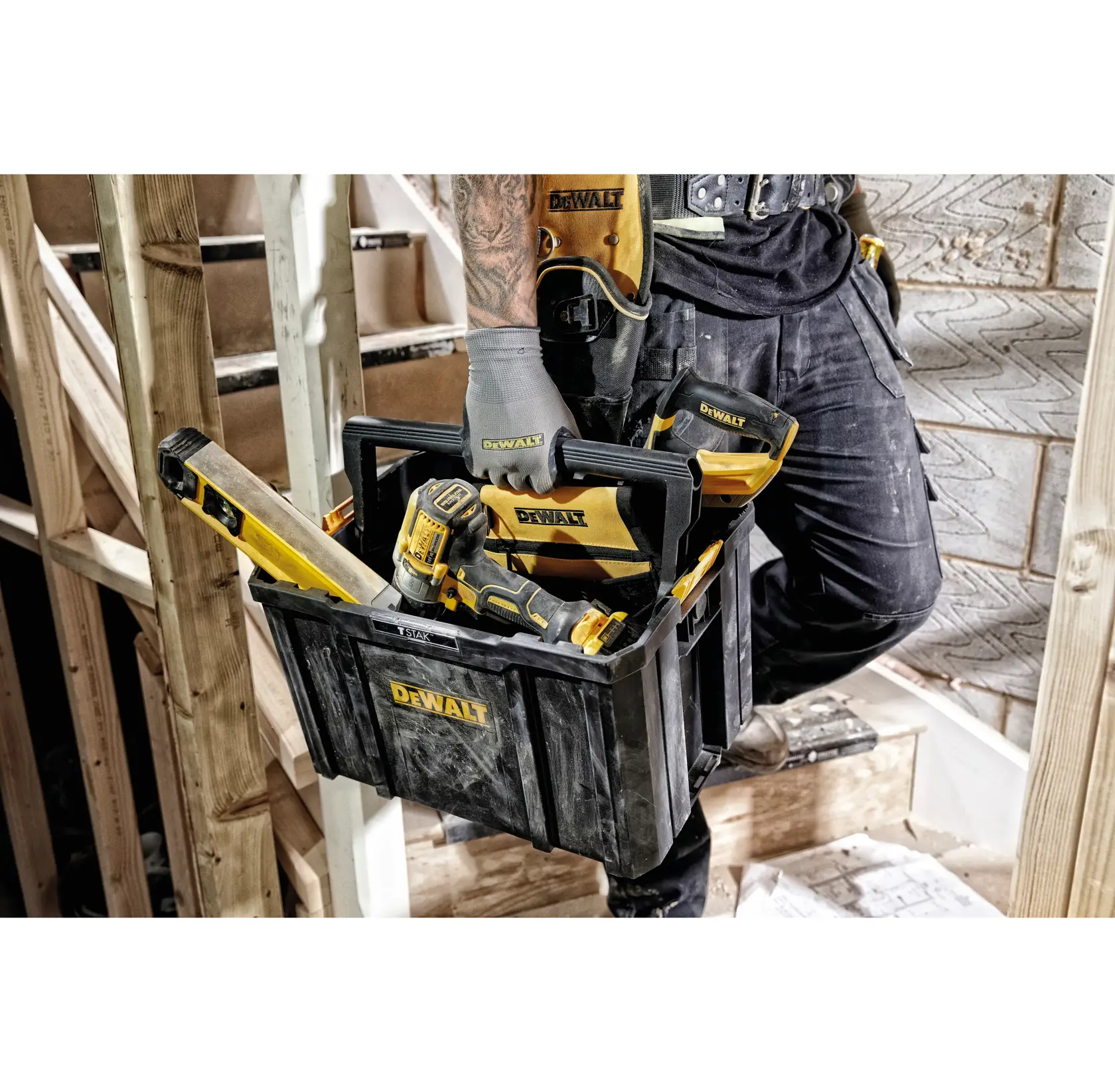 Persona sostiene caja de herramientas DEWALT con herramientas en obra. Incluye taladro y nivel.