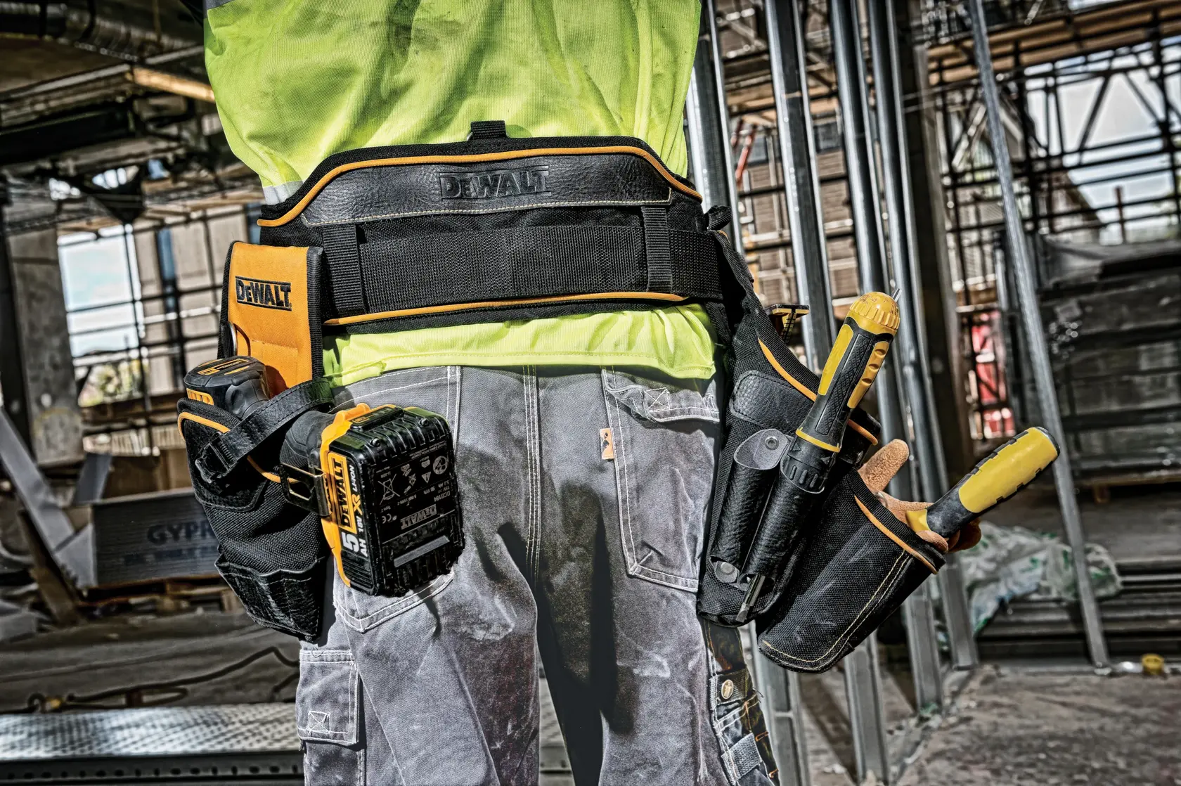 Trabajador con cinturón de herramientas DEWALT y varios utensilios en obra.