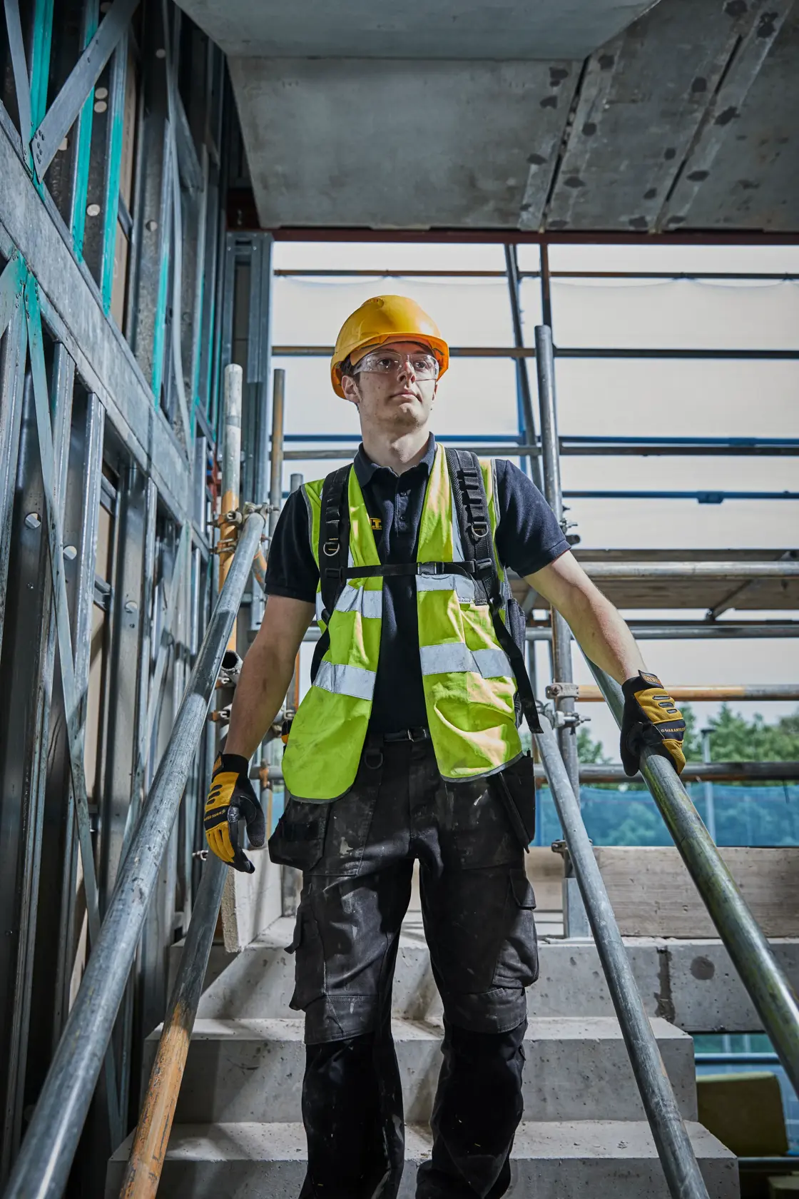 Person in safety gear and gloves walking on stairs at construction site with metal scaffold.