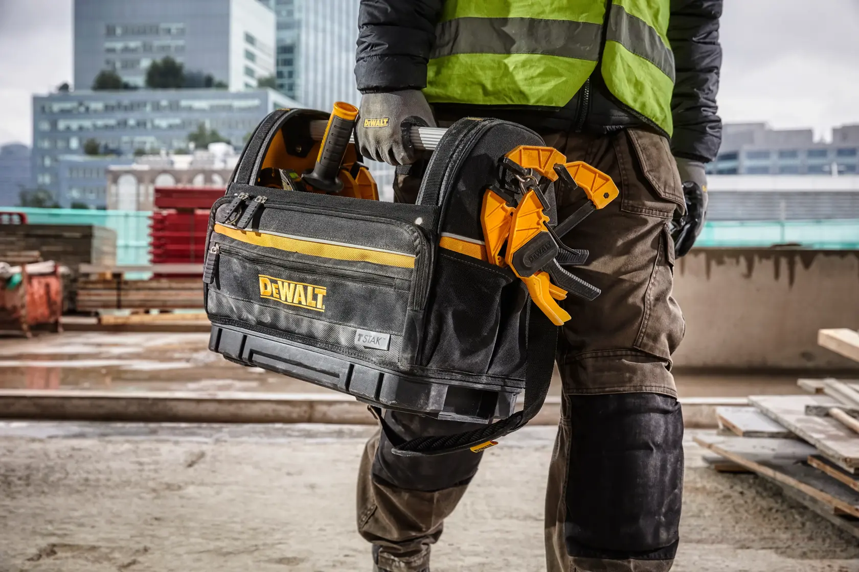 Persona llevando bolsa DEWALT con herramientas en obra, usando ropa y guantes de protección.