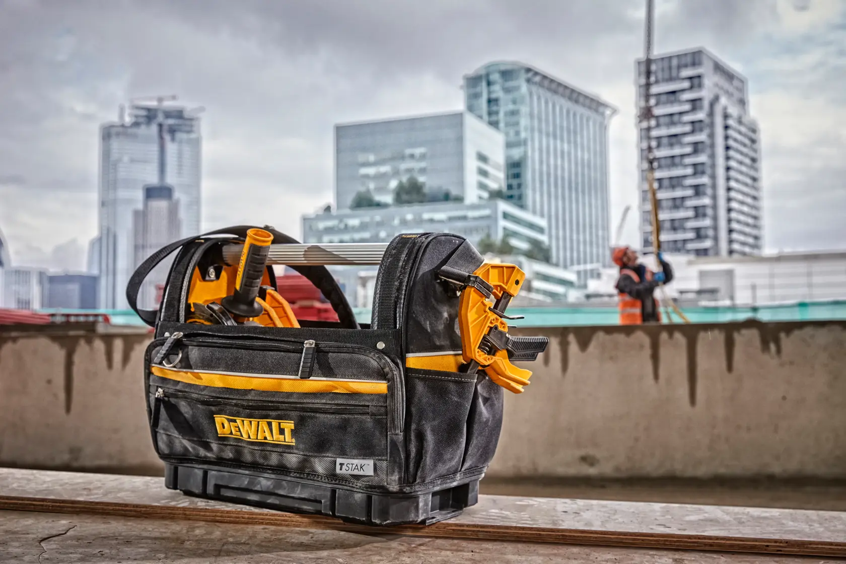 Bolsa de herramientas DEWALT con herramientas en obra, edificios de ciudad al fondo.