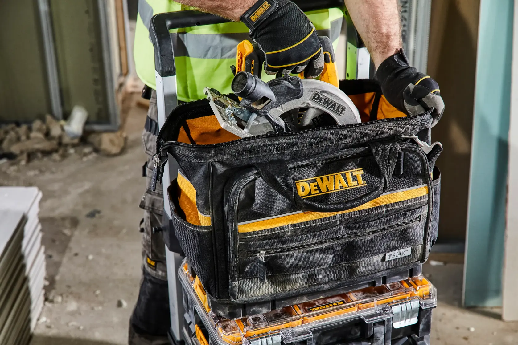 Bolsa DEWALT con sierra circular y herramientas en obra. Persona con guantes y chaleco maneja herramientas.