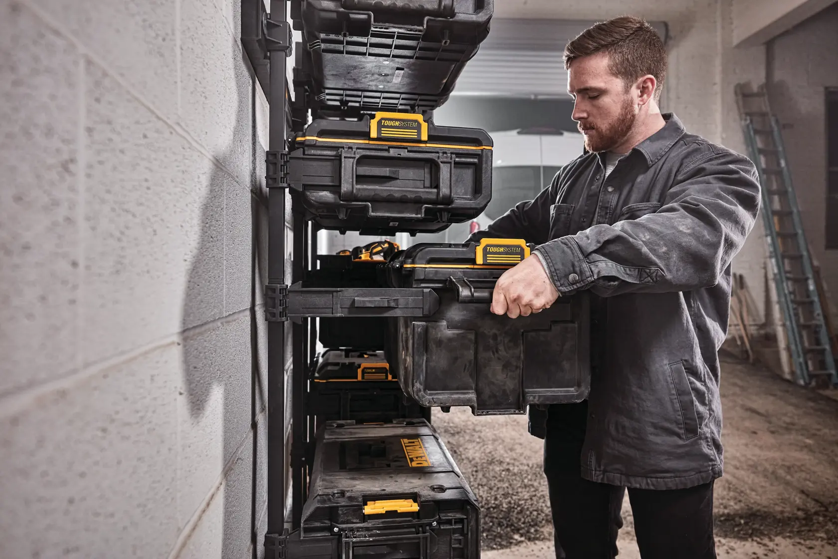 Person stellt einen DEWALT Werkzeugkasten auf ein Regal in einer Werkstatt. Mehrere Kästen sind sichtbar.