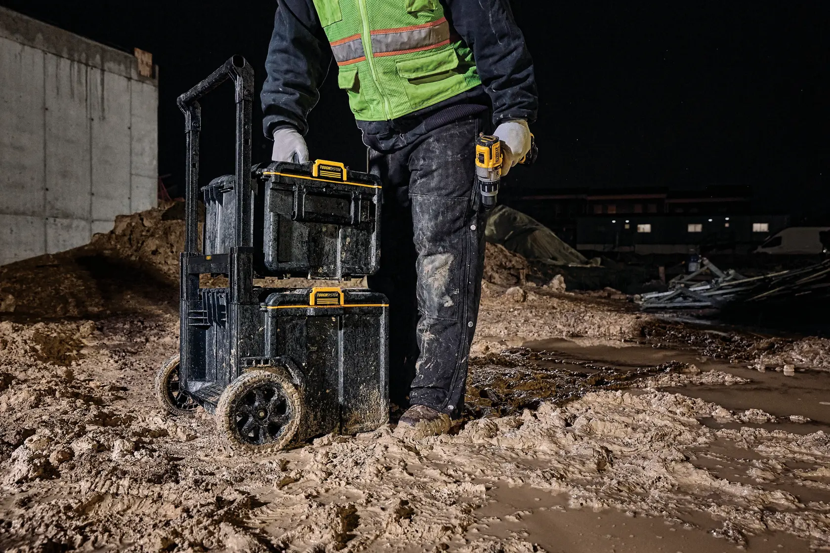 Arbeiter mit DEWALT Werkzeugkisten auf Rädern nachts auf schlammiger Baustelle.