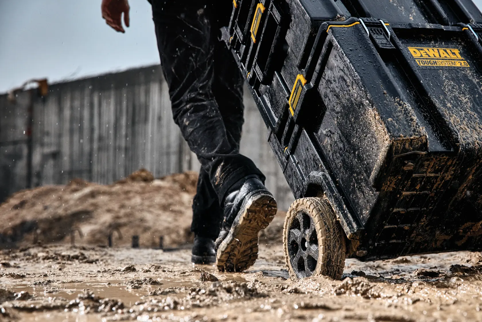 Schlammige DEWALT ToughSystem 2.0 Werkzeugbox auf Rädern auf nasser Baustelle.