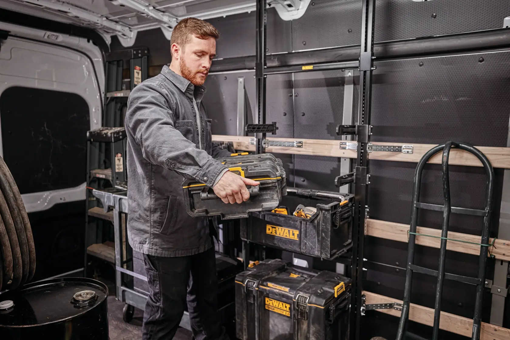 Persona organiza cajas DEWALT en una furgoneta de trabajo con estantes y equipos visibles al fondo.