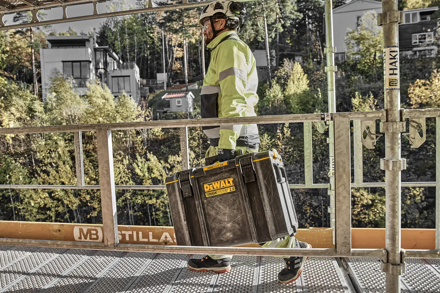 Persona con equipo de seguridad lleva una caja DEWALT Toughsystem 2.0 en obra.