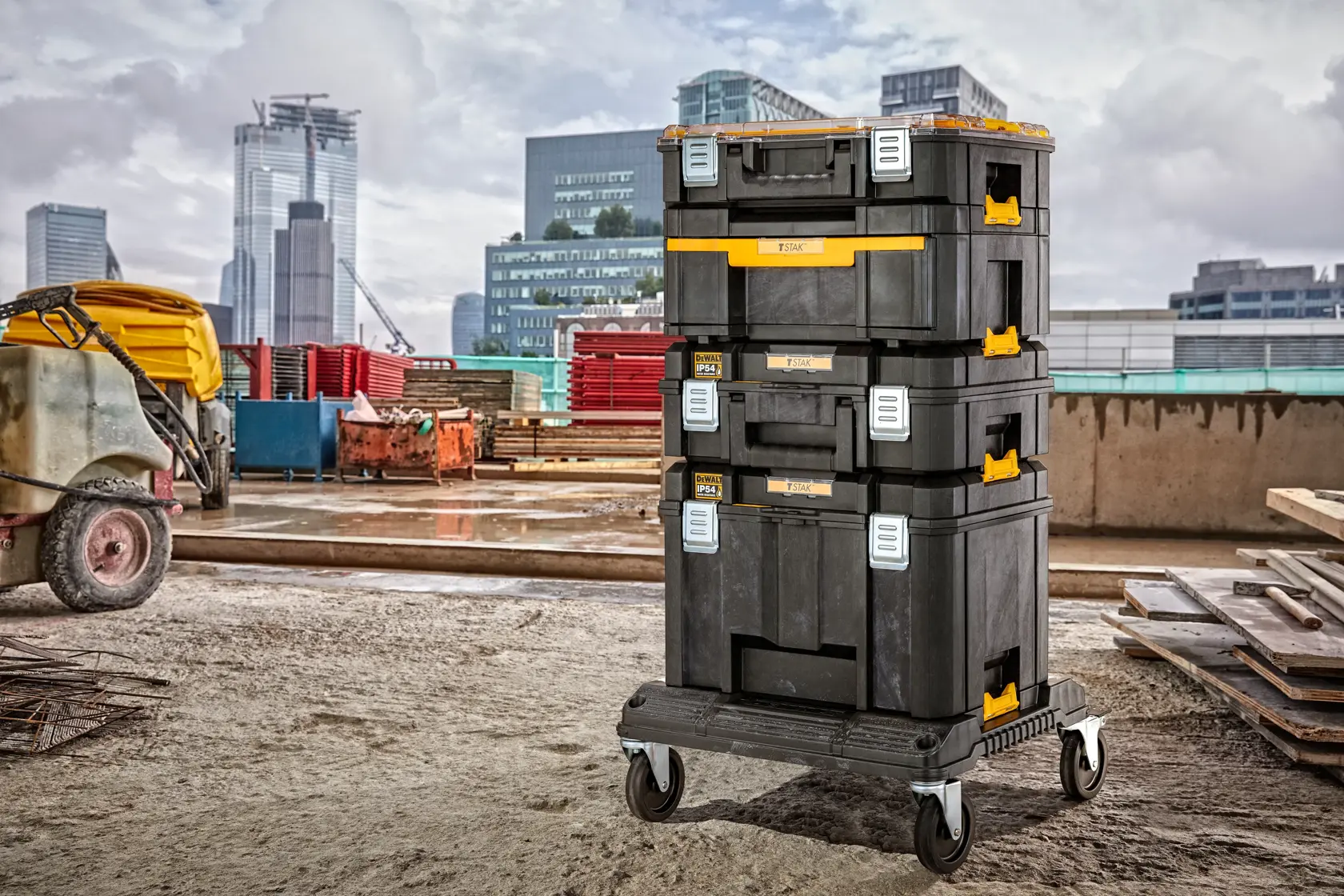 Cajas de herramientas DEWALT apiladas sobre ruedas en obra, con edificios al fondo.