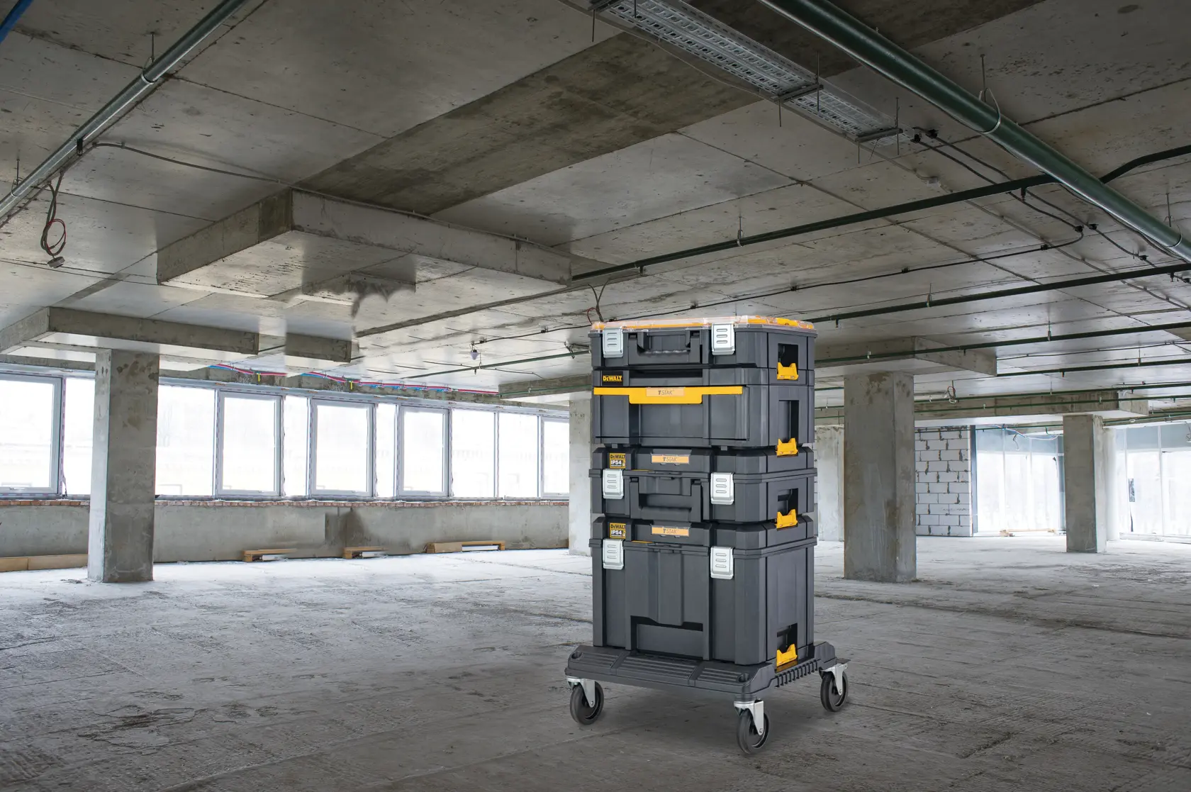 Cajas DEWALT apiladas en carrito en edificio sin terminar con suelo y techo de hormigón.