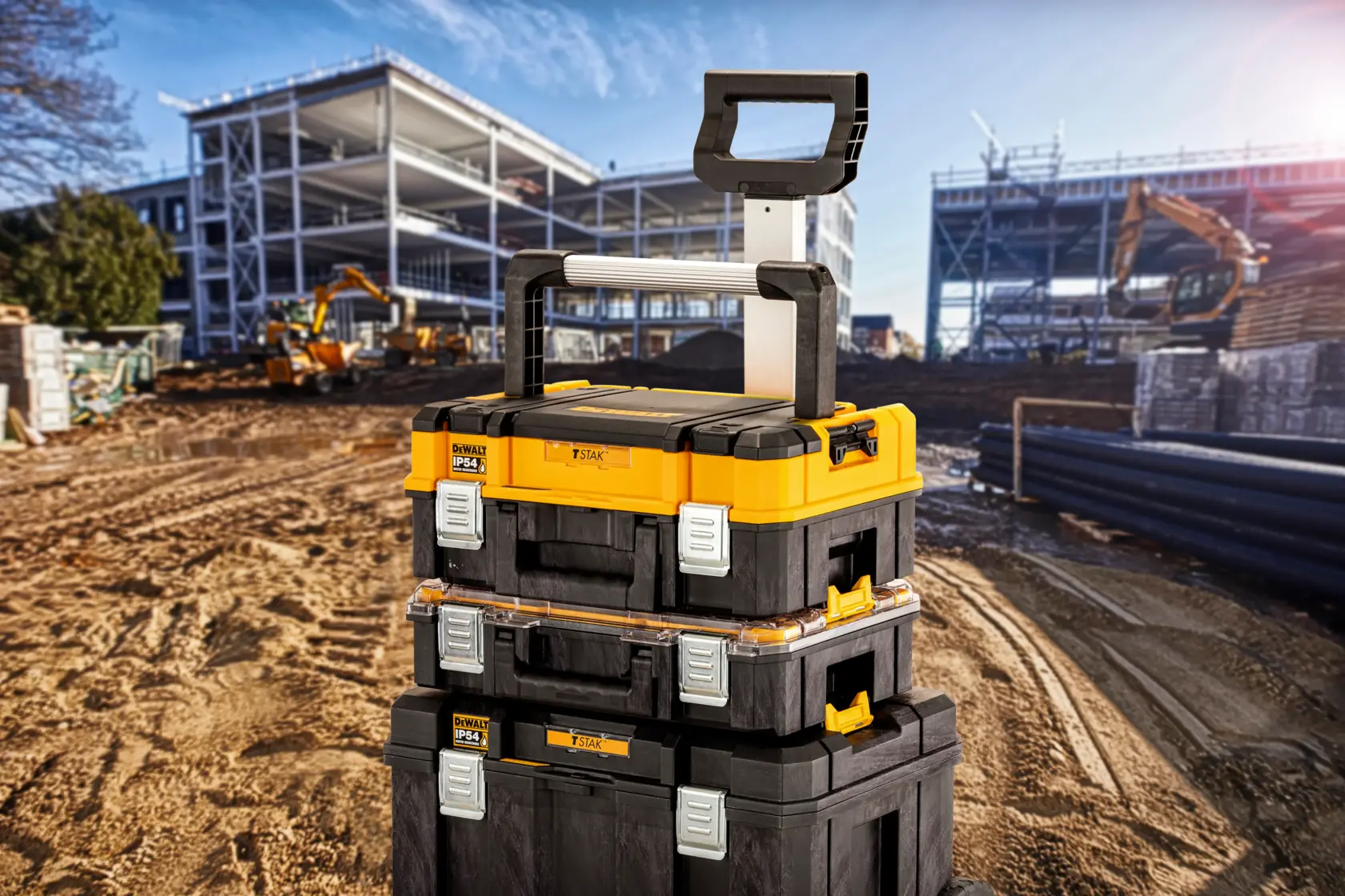 Cajas de herramientas DEWALT apiladas con asa en obra, estructuras metálicas y maquinaria al fondo.