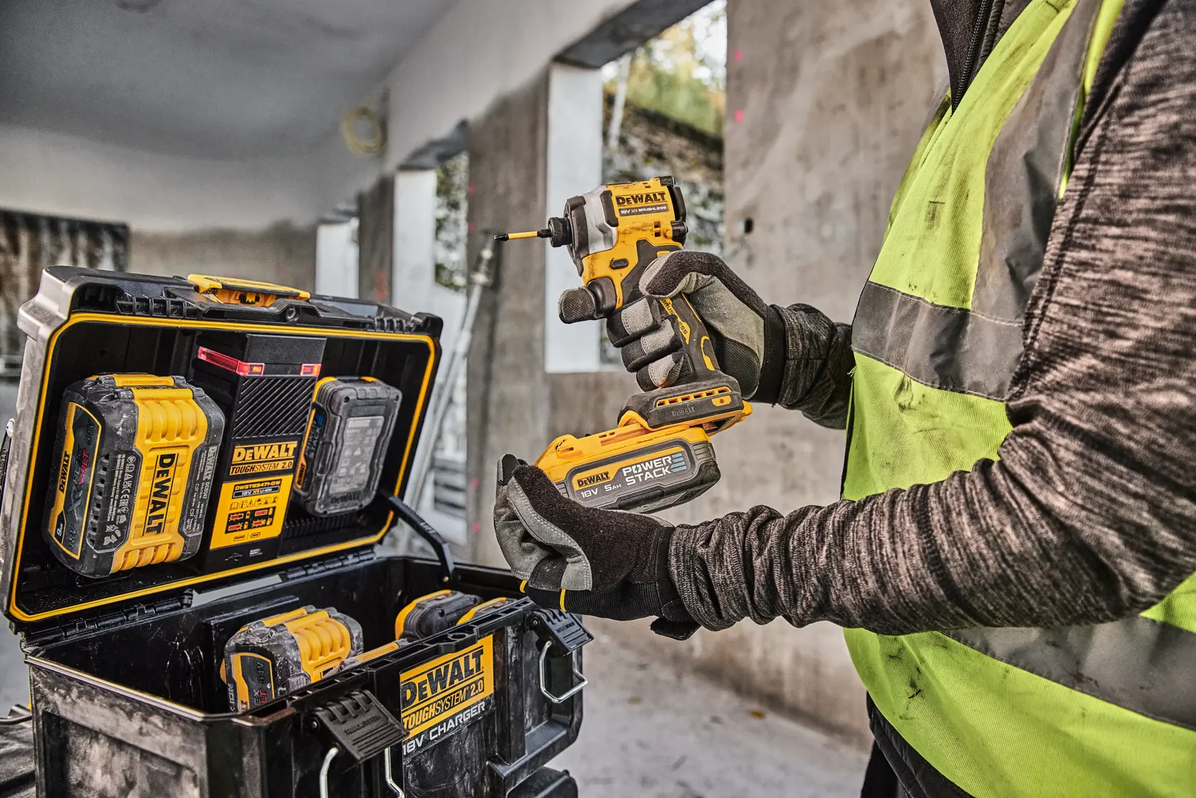 Person hält DEWALT Werkzeug und Akku, DEWALT Werkzeugkoffer und Akkus auf Baustelle sichtbar.