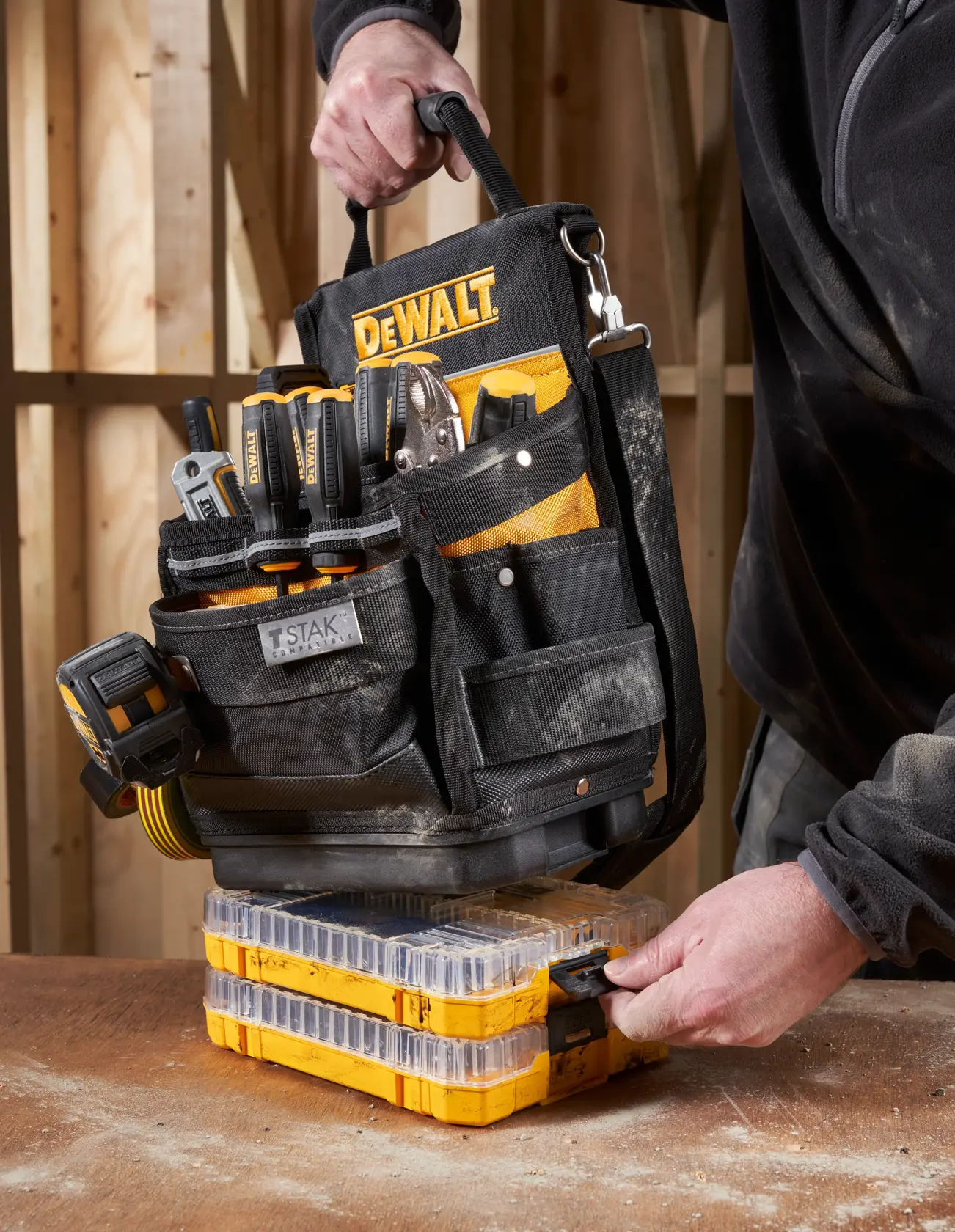 DEWALT Werkzeugtasche mit Werkzeugen auf gelben stapelbaren Boxen, gehalten von einer Person in Arbeitskleidung.