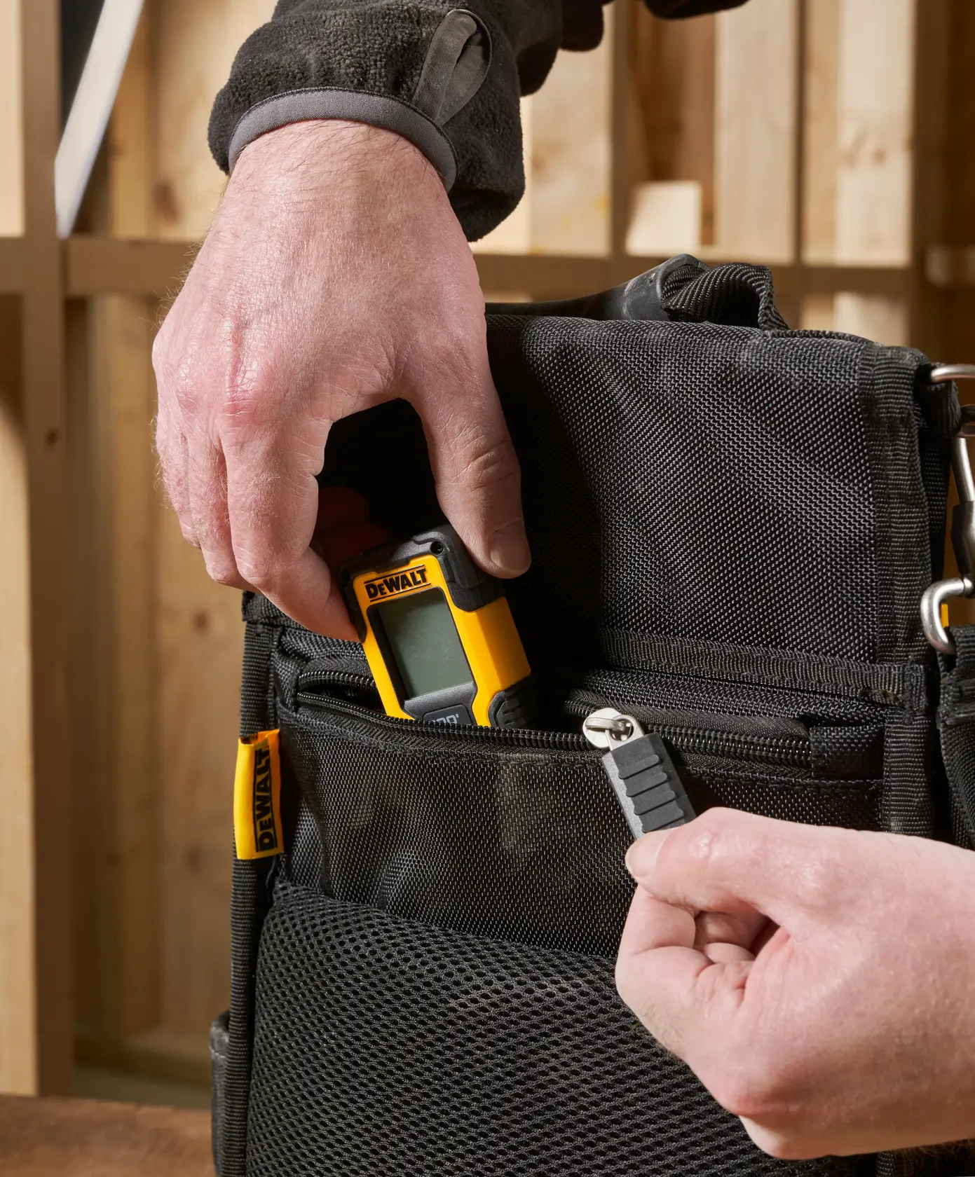 Hand legt DEWALT-Gerät und Bit in schwarze Taschen mit Reißverschluss, Werkstattumgebung.