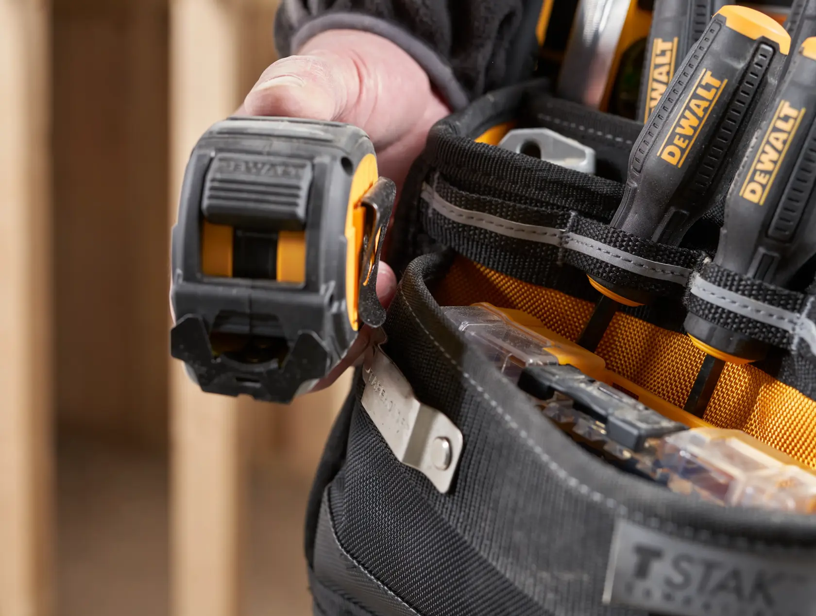 Detailaufnahme eines DEWALT Werkzeuggürtels mit Hand, Maßband und Schraubendrehern.